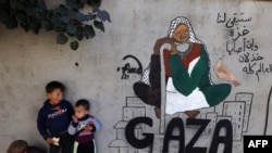 Displaced Palestinian children stand next to a mural painting by artist Amal Abo in Rafah in the southern of Gaza Strip, on Dec. 31, 2023.