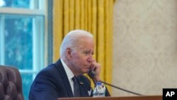 FILE - In this photo taken through a window, President Joe Biden talks on the phone in the Oval Office of the White House in Washington, Dec. 9, 2021.