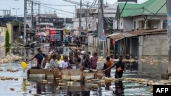 People cross floodwaters in the Pompage district in Kinshasa, Democratic Republic of Congo, on Jan. 9, 2024, following heavy rains. Regional flooding left some 350,000 people in need of humanitarian aid in neighboring Republic of Congo.