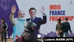 Seorang pria melewati papan reklame bergambar Presiden Prancis Emmanuel Macron (3 kanan) dan Perdana Menteri India Narendra Modi (2 kiri), di Jaipur pada 25 Januari 2024. (Foto: Ludovic MARIN/POOL/AFP)