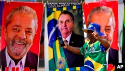 A demonstrator dressed in the colors of the Brazilian flag stands in front of towels for sale featuring Brazilian presidential candidates current President Jair Bolsonaro, center, and former President Luiz Inacio Lula da Silva, in Brasilia, Brazil, Sept. 