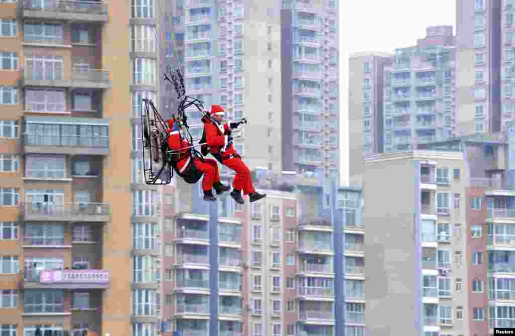 Members of a local powered parachute club wearing Santa Claus costumes fly past residential buildings to drop presents to pedestrians during a promotional event celebrating Christmas in Guiyang, Guizhou province December 24, 2014. Picture taken December 2