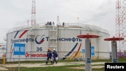 Workers walk past a storage tank at the Kaleikino oil pumping station of Transneft Kama Region near Almetyevsk, Russia, April 27, 2022.