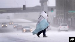 A person wrapped in a blanket crosses a snow-covered street, Dec. 22, 2022, in St. Louis. Snow and frigid temperatures have moved across the U.S., complicating holiday travel and plans in the coming days.