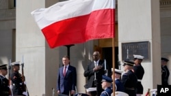 Defense Secretary Lloyd Austin, right, stands with Polish Defense Minister Mariusz Błaszczak, left, as the National Anthem is played during an arrival ceremony at the Pentagon in Washington, Apr. 20, 2022.