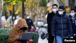 A woman wearing a face mask looks at her laptop on a street, as coronavirus disease (COVID-19) outbreaks continue in Shanghai, China, Dec. 14, 2022.