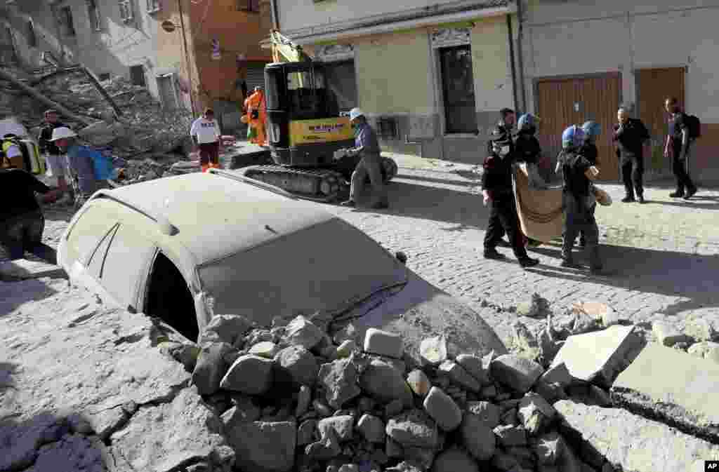 A body is carried away as a car is covered in rubble after an earthquake, in Amatrice, Aug. 24, 2016. A devastating earthquake rocked central Italy early in the morning, collapsing homes on top of residents as they slept.