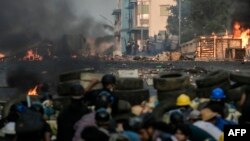 Police officers (background) take position along a road as protesters take cover behind makeshift barricades during a crackdown on demonstrations by protesters against the military coup in Yangon on March 16, 2021. (Photo by STR / AFP)