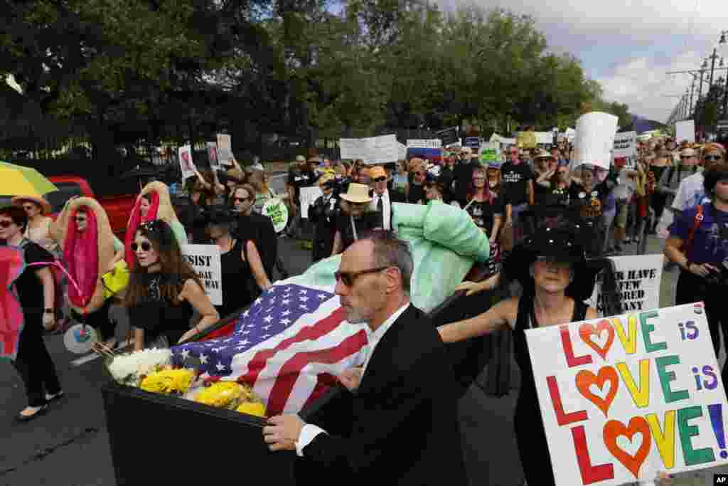 People walk beside a fake Statue of Liberty that has been put in a coffin and covered in an American flag, in protest of the inauguration of Donald Trump, in New Orleans, Louisiana, Jan. 20, 2017.