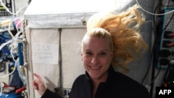 This handout photo released Oct. 22, 2020, by NASA on Twitter shows International Space Station crew member Kate Rubins pointing to a sign reading "ISS voting booth". (AFP)