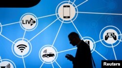 A man looks at his phone in front of a stand at the Mobile World Congress in Barcelona, Spain, showing a variety of devices connected via Wi-Fi and Internet of Things networks, Feb. 28, 2017