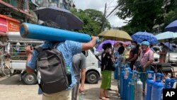 A man carries an oxygen tank while others line up with their oxygen tanks outside an oxygen refill station in Pazundaung township in Yangon, Myanmar, Sunday, July 11, 2021. Myanmar is facing a rapid rise in COVID-19 patients and a shortage of oxygen supplies just as the country i