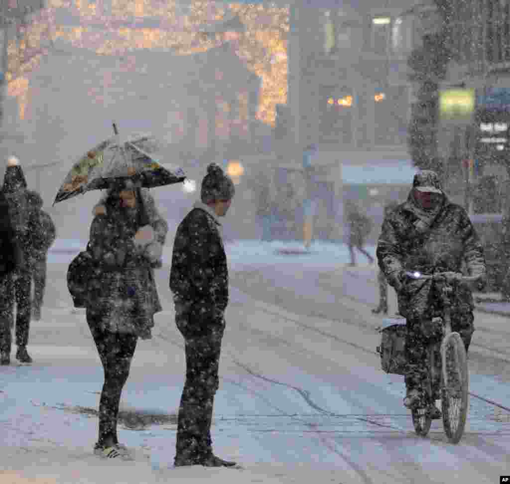 FILE - Two pedestrians wait for a bicycle to pass before crossing a snow-covered shopping street in Amsterdam, Netherlands, Monday, Dec. 11, 2017.