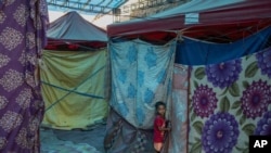 A young Rohingya refugee boy stands outside a tent at a refugee camp alongside the banks of the Yamuna River in the southeastern borders of New Delhi, sprawling Indian capital, July 1, 2021