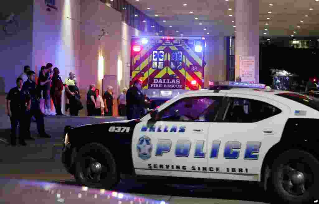 A Dallas police vehicle follows behind an ambulance carrying a patient to the emergency department at Baylor University Medical Center, as police and others stand near the emergency entrance early Friday, July 8, 2016.