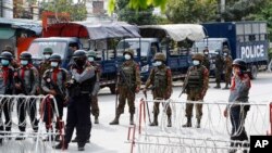 Armed police and soldiers stand guard behind a road barricade with razor wire in Mandalay, Myanmar Friday, Feb. 19, 2021. A young woman who was shot in the head by police during a protest last week against the military's takeover of power in Myanmar died Friday morning, her broth