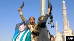 Protesters, one holding a portrait of Huthi leader Abdul Malik al-Houthi (L), brandish their weapons during a protest following US and British forces strikes, in the Huthi-controlled capital Sanaa on January 12, 2024 amid the ongoing battles between Israe