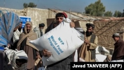 Warga Afghanistan membawa karung-karung berisi makanan yang dibagikan sebagai bantuan Program Pangan Dunia (WFP) di Kandahar pada 19 Oktober 2021. (Foto: AFP/Javed Tanveer)