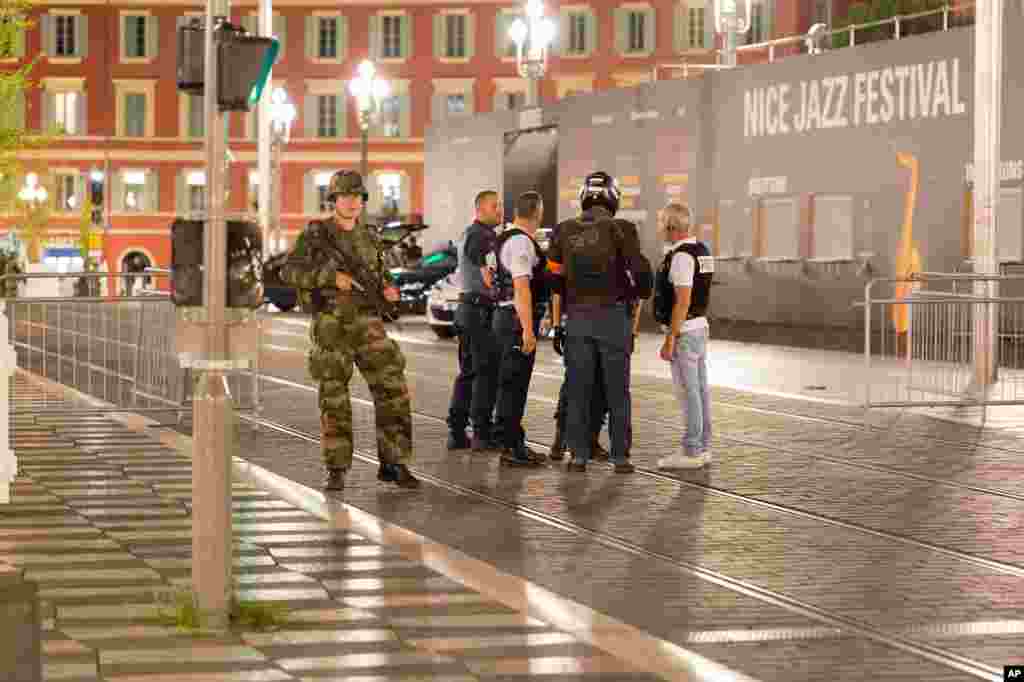 Police officers and a soldier stand by the sealed off area of an attack after a truck drove on to the sidewalk and plowed through a crowd of revelers who'd gathered to watch the fireworks in the resort city of Nice, southern France, July 15, 2016.