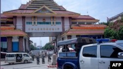 Chinese border police guards keep watch as migrant workers return from China at the Myanmar border gate in Muse in Shan state on May 12, 2020. - Hundreds of migrant workers, who had been trapped in China as a result of the COVID-19 novel coronavirus pande