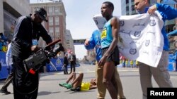 Winner of the men's division Lelisa Desisa Benti of Ethiopia (R) is wrapped in a towel as third place finisher compatriot Gebregziabher "Gebre" Gebremariam (C) lays on the ground during the 117th Boston Marathon in Boston, Massachusetts April 15, 2013. RE