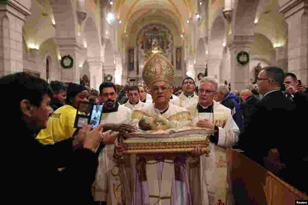 The Latin Patriarch of Jerusalem Fouad Twal carries a statuette of baby Jesus during a Christmas Midnight Mass at the Church of the Nativity in the West Bank town of Bethlehem, Dec. 25, 2014. 