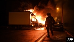 A French anti riot police officer walk past a burning truck in Nantes, western France on early July 1, 2023, four days after a 17-year-old man was killed by police in Nanterre, a western suburb of Paris.