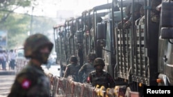 FILE- Soldiers stand next to military vehicles as people gather to protest against the military coup, in Yangon, Myanmar, Feb. 15, 2021.