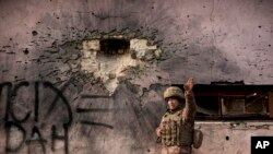 A Ukrainian serviceman points to the direction of the incoming shelling next to a building which was hit by a large caliber mortar shell in the frontline village of Krymske, Luhansk region, in eastern Ukraine, Feb. 19, 2022. 