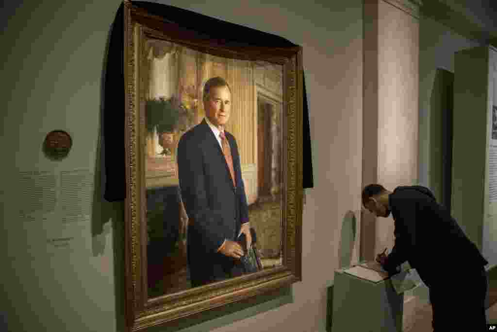 Ameer Hassan of New York stops to sign the condolence book as the official portrait of former President George H.W. Bush is draped in black cloth at the National Portrait Gallery in Washington, Dec. 3, 2018, to mark his passing.