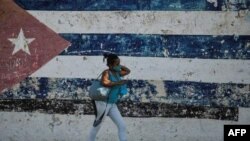 In this file photo taken on June 22, 2021 a woman walks near a wall depicting the Cuban flag in Havana. (Photo: AFP)