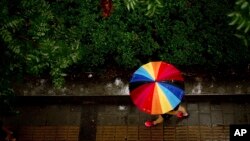 A woman carries a rainbow-colored umbrella as she walks during a rain shower in Beijing.